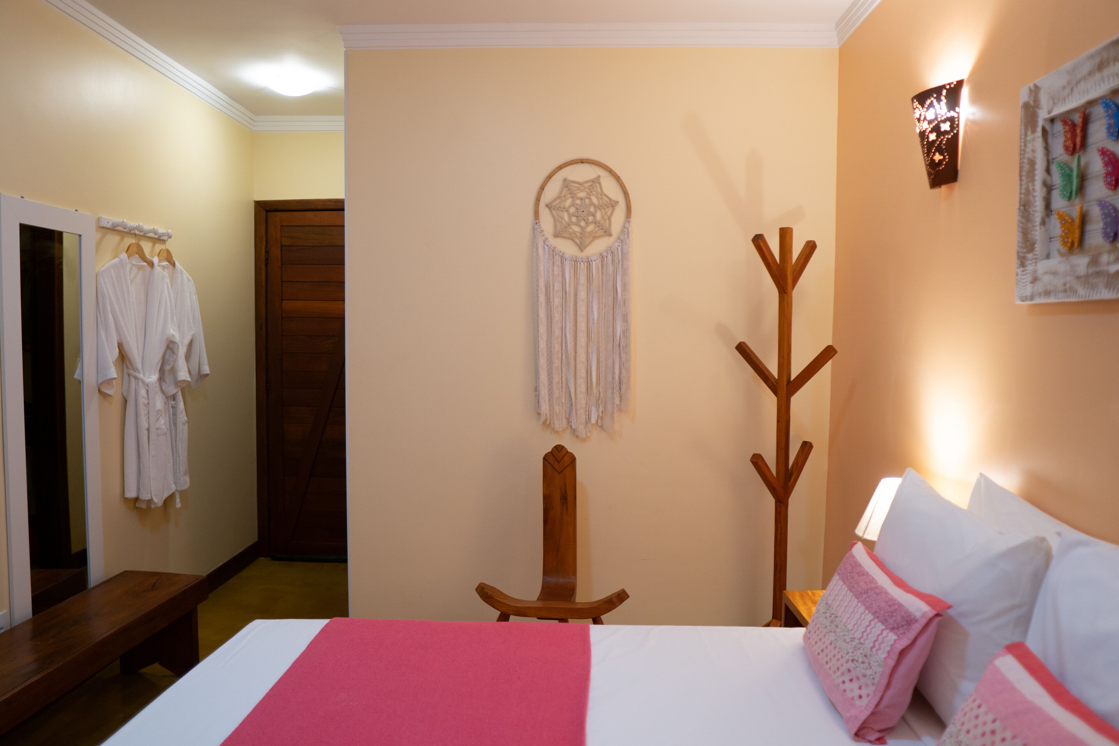 A hotel room with a bed, a wooden coat rack, a dreamcatcher, and a wall-mounted artwork.