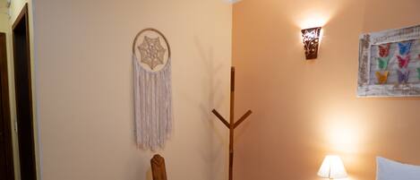 A bedroom with a bed, a nightstand with a lamp, a wooden chair, a dreamcatcher, and wall art.