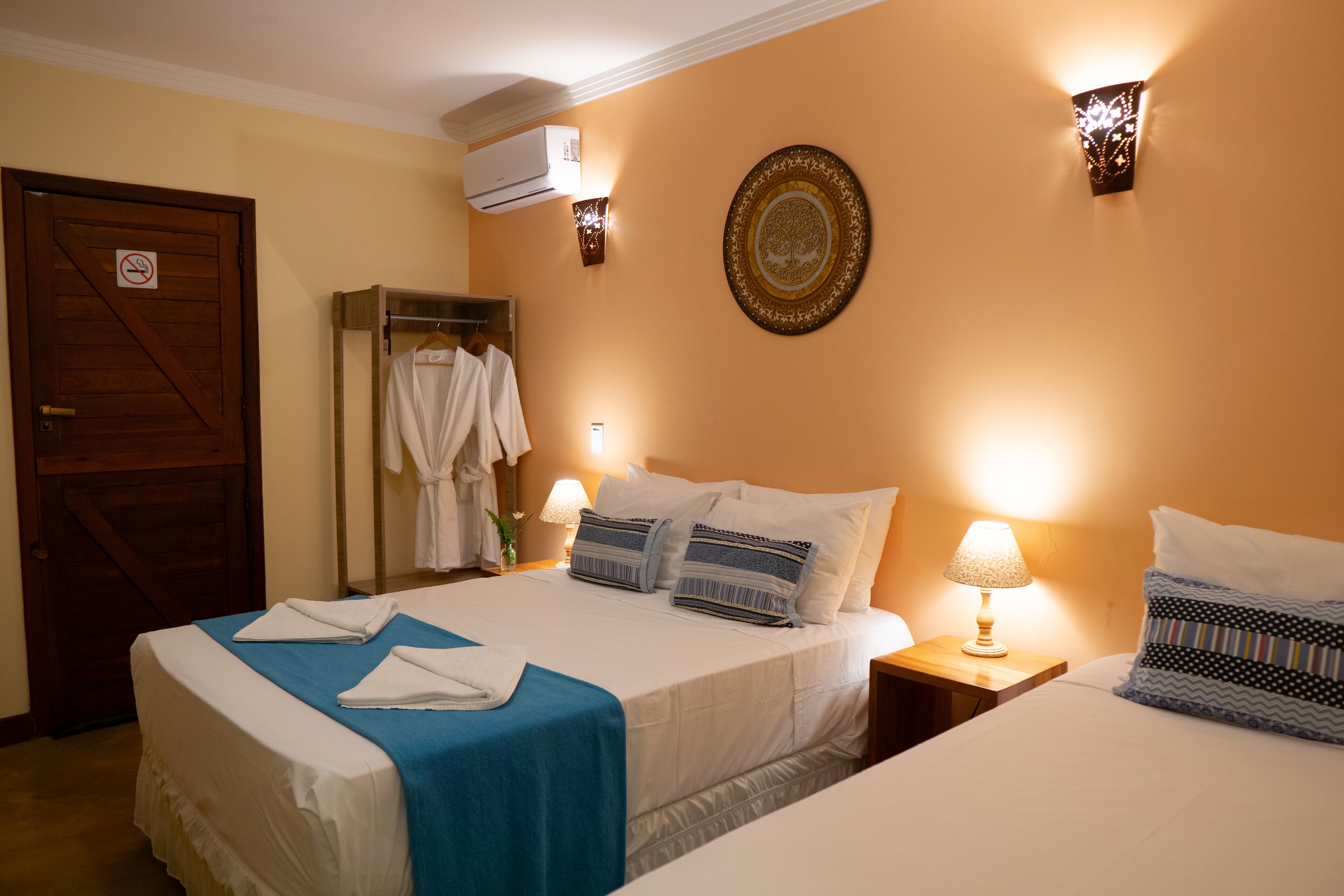 Quarto de hotel com duas camas, um guarda-roupa, um espelho, um ar condicionado fixado na parede e um prato decorativo.