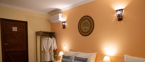 Quarto de hotel com duas camas, um guarda-roupa, um espelho, um ar condicionado fixado na parede e um prato decorativo.