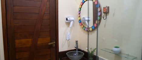A bathroom with a wooden door, a glass sink, a mirror with a flower frame, and a hairdryer on the wall.