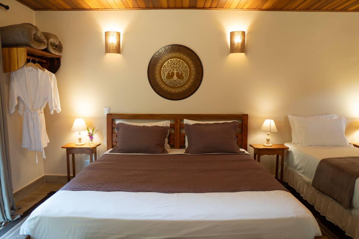 Quarto de hotel com uma cama grande, duas mesas de cabeceira com luminárias, uma cabeceira de madeira e um prato decorativo na parede.