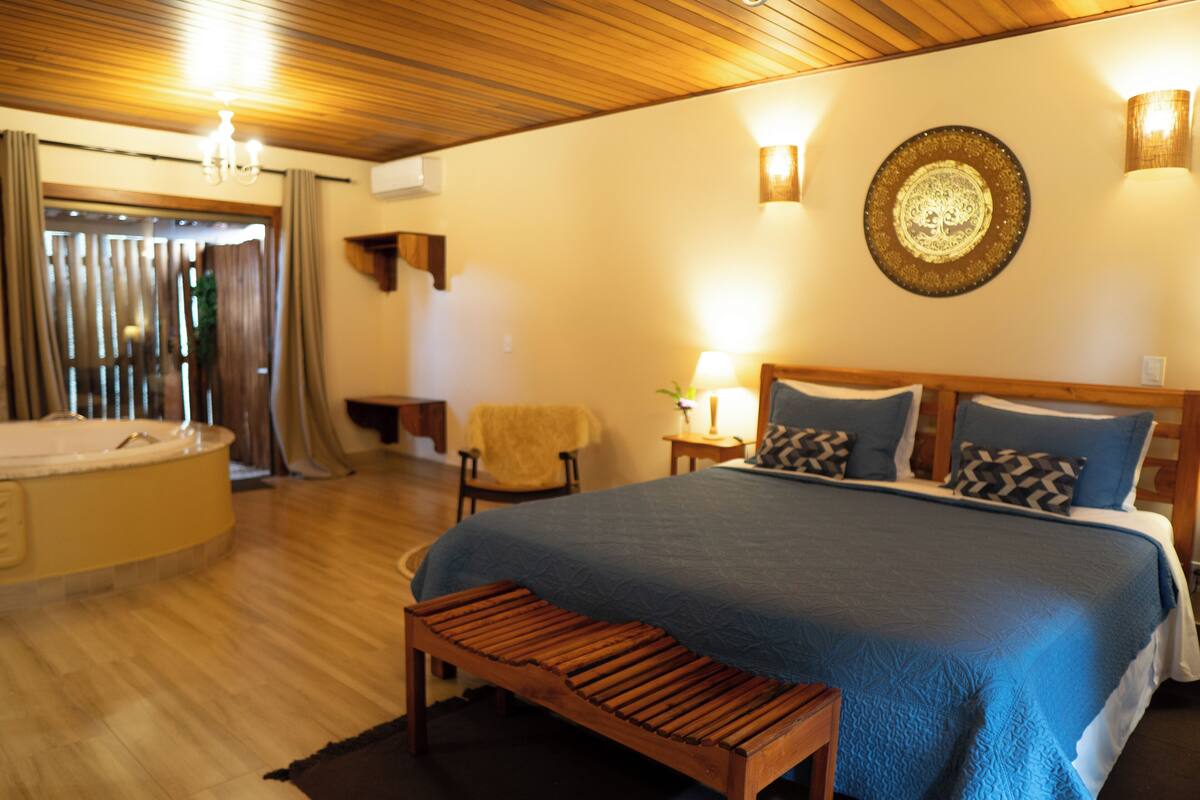 Quarto com uma cama grande, um banco de madeira, uma banheira e um candeeiro fixado na parede.