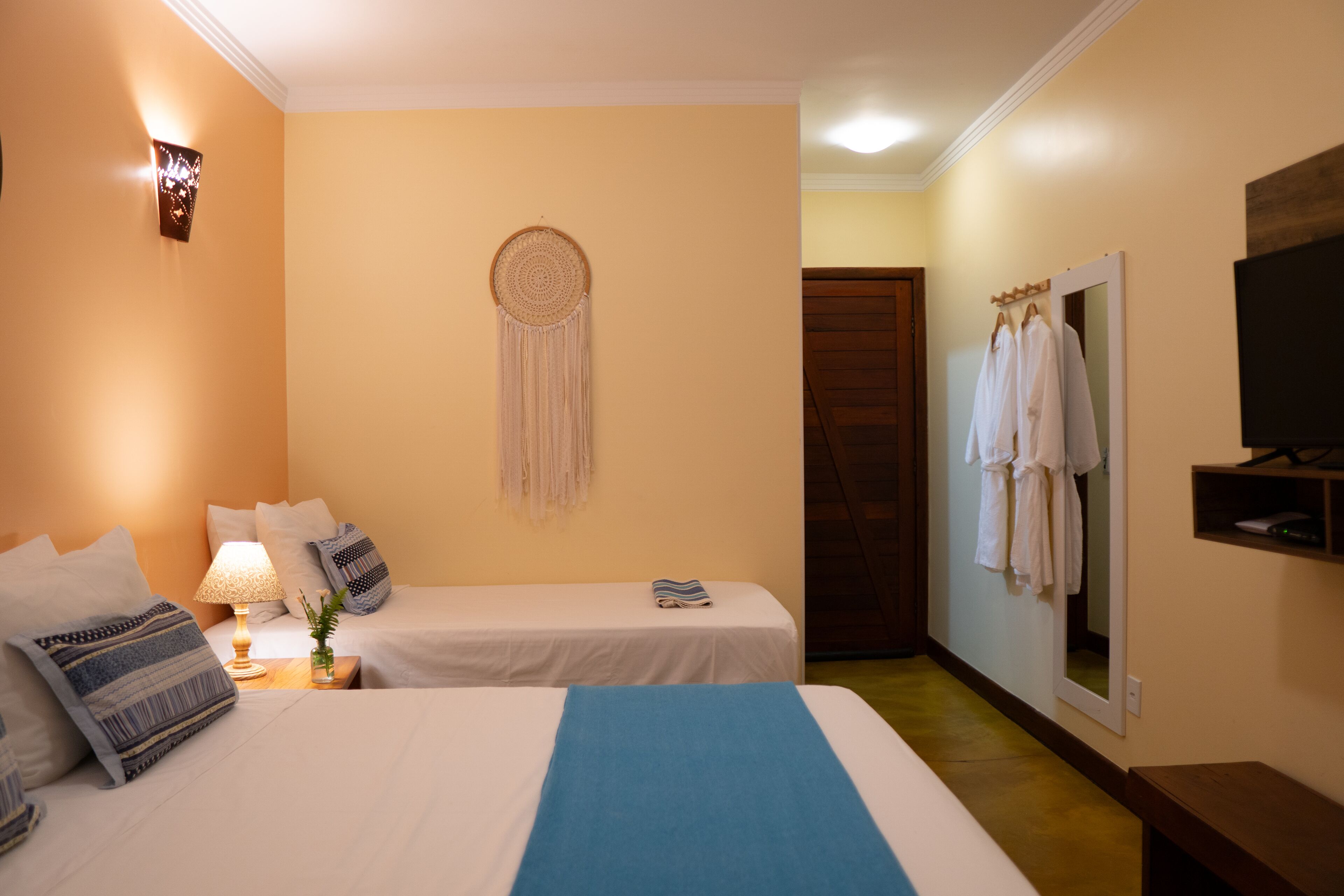 Une chambre d’hôtel avec deux lits, un attrape-rêves fixé au mur, un miroir et une télévision.