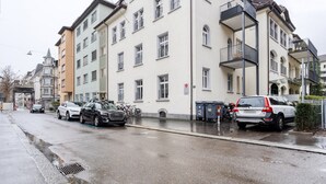 Eine Straße mit parkenden Autos und einem mehrstöckigen Gebäude mit Balkonen.