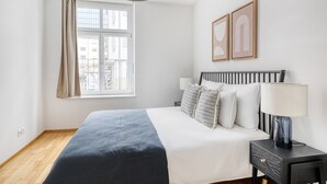 Ein Schlafzimmer mit Bett, Nachttisch, Lampe und einem Fenster mit Vorhängen.