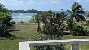 Une vue sur une plage tropicale, avec des palmiers, un ciel dégagé et un bâtiment situé au loin.