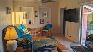 Un salon chaleureux avec des meubles en osier, un téléviseur à écran plat et un tapis aux motifs tropicaux.