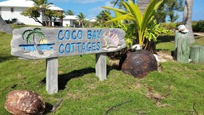 Une enseigne en bois indiquant « Coco Bay Cottages », avec un palmier et des coquillages.