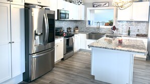 Una cocina moderna con electrodomésticos de acero inoxidable, armarios blancos, una isla con encimera de granito y una lámpara colgante.