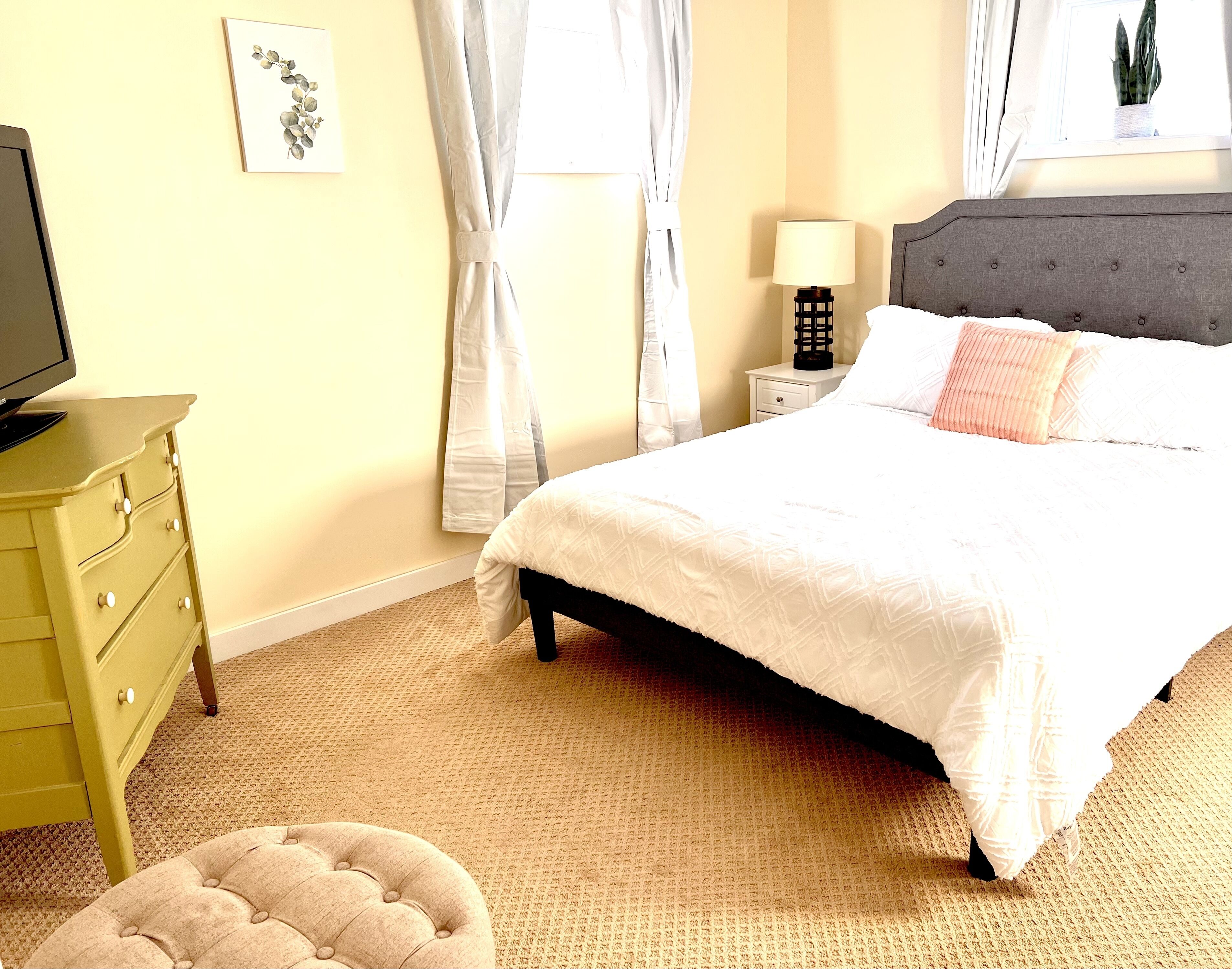 A bedroom with a bed, a nightstand, a lamp, a dresser, and a television.