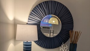 Une console blanche, ornée d’une lampe, d’un miroir décoratif et d’un vase contenant des roseaux.