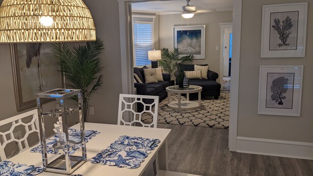 Un coin repas avec une table dressée pour deux personnes, un luminaire suspendu et une vue sur le salon.