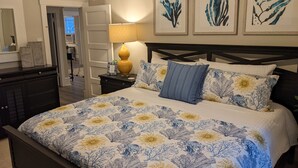 Une chambre à coucher avec un grand lit, une table de chevet avec une lampe et trois œuvres d’art encadrées accrochées au mur.