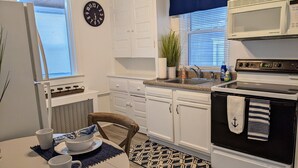 Una cocina con armarios blancos, microondas, estufa, fregadero y un reloj en la pared.