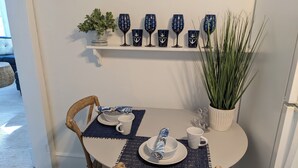 Una mesa de comedor dispuesta con platos blancos, servilletas azules y un paraguas azul. Seis copas de vino con diseños de anclas en la pared de arriba.