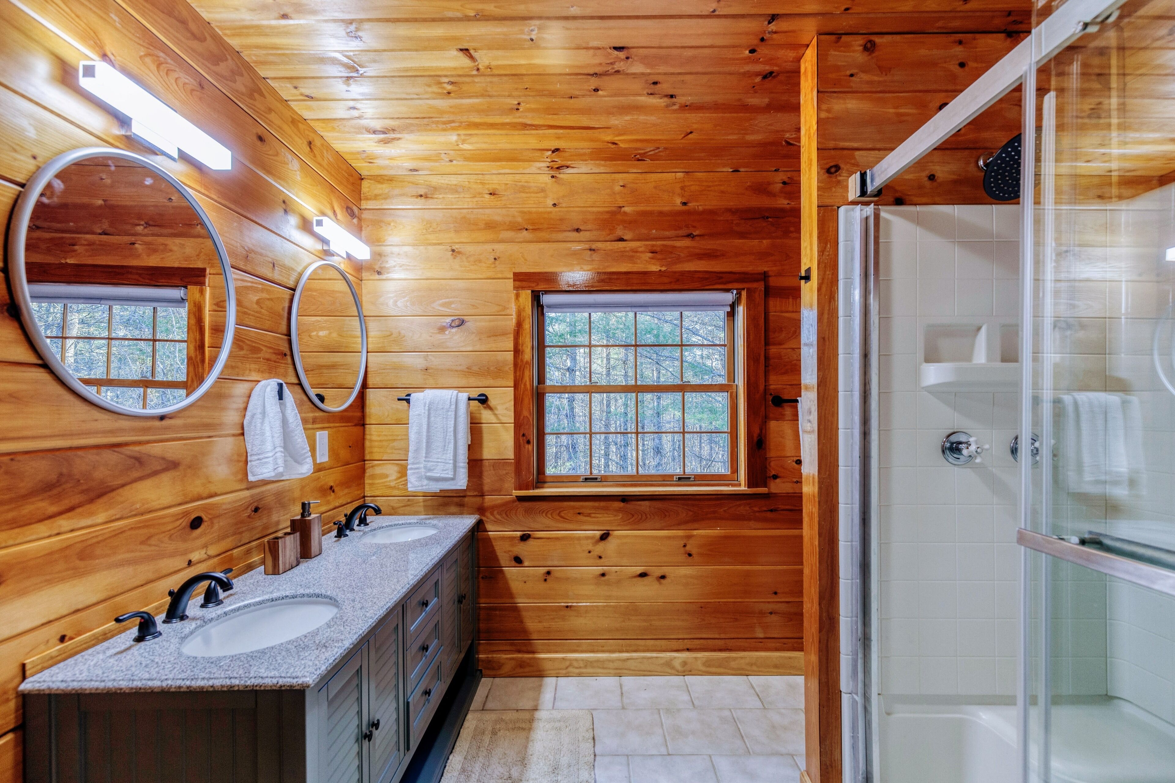 Une salle de bain rustique, avec deux lavabos, une douche et deux fenêtres.