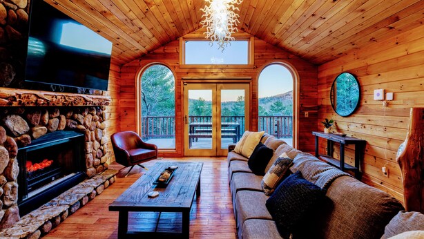 L’intérieur d’un chalet confortable, avec une cheminée en pierre, un plafond en bois et un grand téléviseur.
