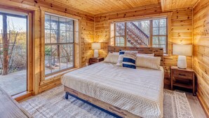 Une chambre située dans une cabane en bois, avec un grand lit, deux tables de chevet et une fenêtre donnant sur un escalier en bois.