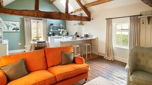 A cozy living room with a bright orange sofa, a green armchair, and a wooden ceiling. - A romantic getaway, with access to the well known Mortimer Walking Trail.  (Leominster)