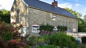 A stone house with a sloped roof, white windows, and a garden with various plants and flowers. - A romantic getaway, with access to the well known Mortimer Walking Trail.  (Leominster)