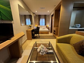 A hotel room with a bed, a desk, a TV, a sofa, and a coffee table with flowers. - De Palma Resort Kuala Selangor (Kuala Selangor)