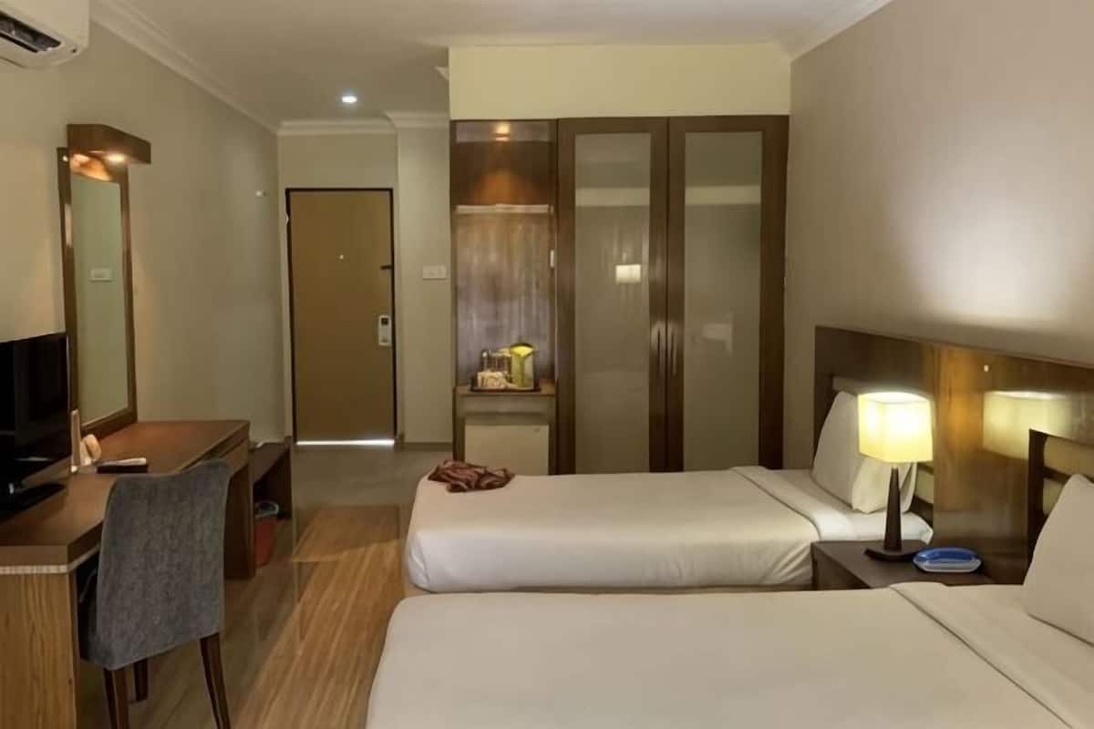Ein Hotelzimmer mit zwei Betten, einem Schreibtisch mit Stuhl, einem Fernseher, einem Kleiderschrank und einem Nachttisch mit Lampe.