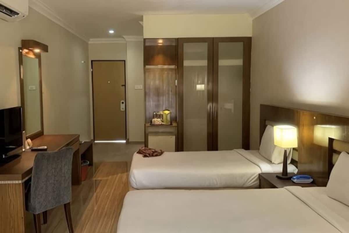 Une chambre dâhĂŽtel avec deux lits, un bureau avec une chaise, une tĂ©lĂ©vision, une armoire et une table de chevet avec une lampe.