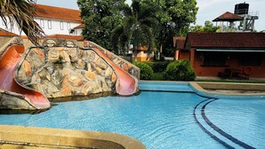 A swimming pool with a slide, stone wall, and tiled deck. - De Palma Resort Kuala Selangor (Kuala Selangor)