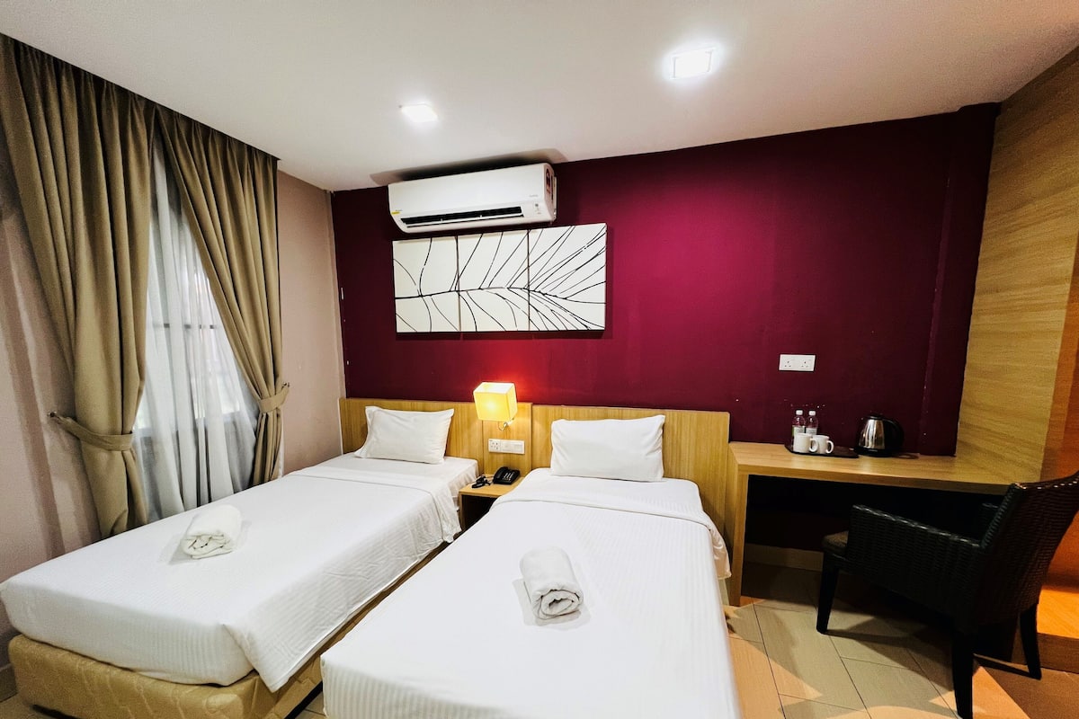 Ein Hotelzimmer mit zwei Einzelbetten, einem Schreibtisch, einem Stuhl, einer Klimaanlage und einem Wandbild.