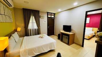 A hotel room with a bed, a desk with a television, a small trash bin, and a door leading to another room.