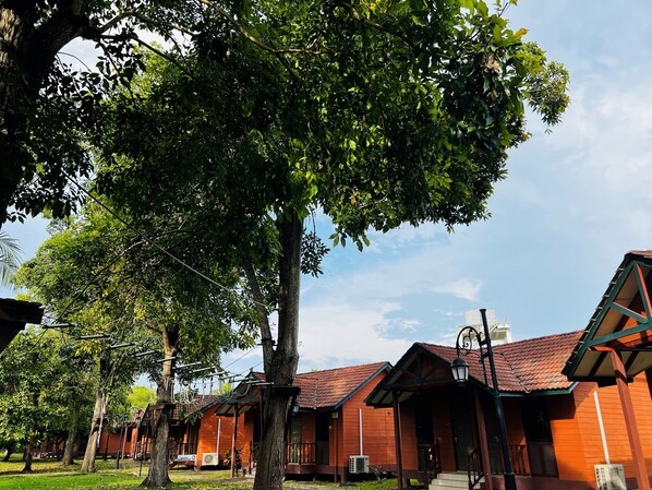 A row of wooden cabins with a large tree in the foreground. - De Palma Resort Kuala Selangor (Kuala Selangor)