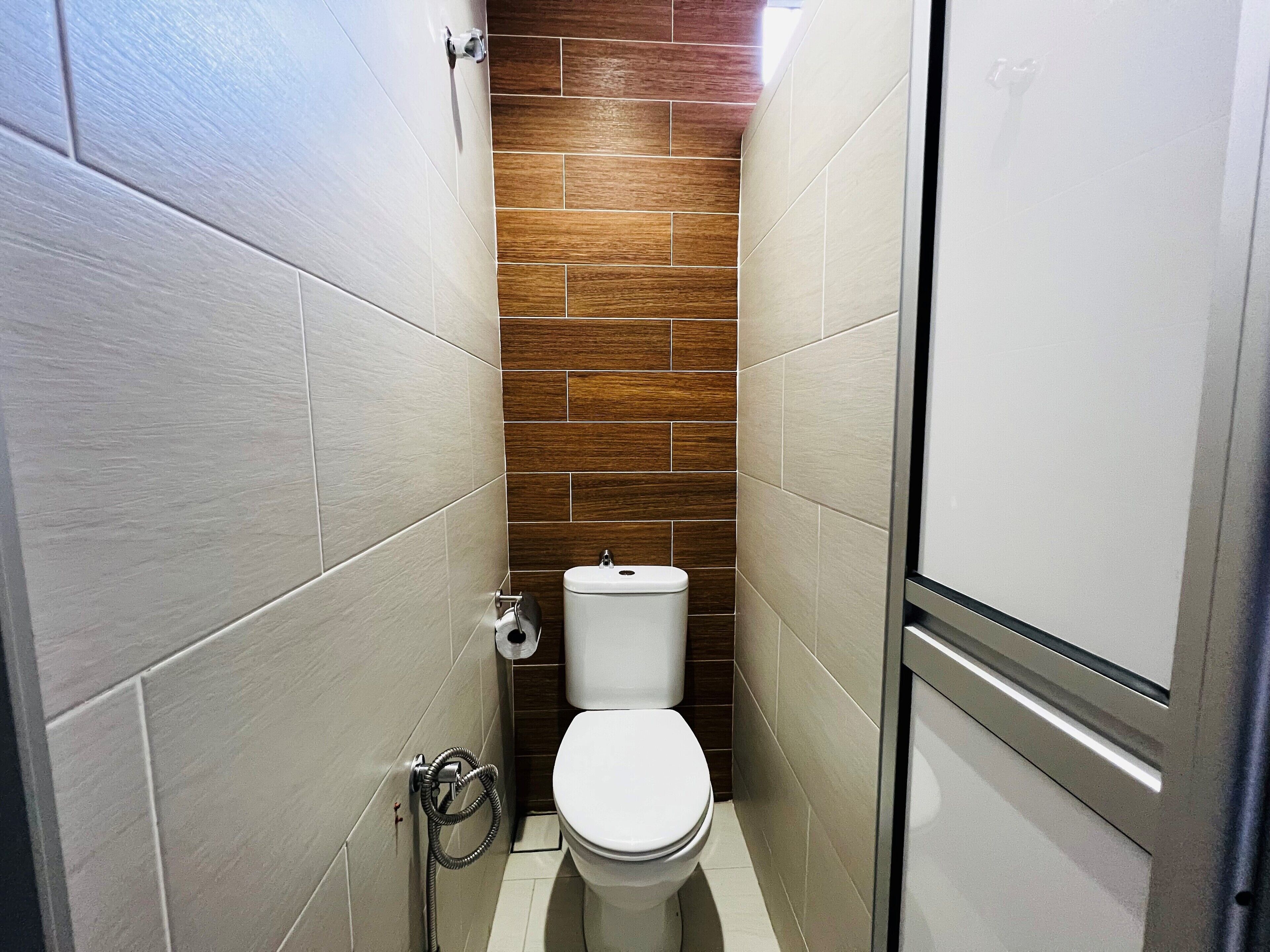 A small, modern bathroom with a white toilet, a wooden accent wall, and a shower area.