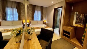 A hotel room with a large bed, a wooden dining table with flowers, a chair, a small table with a lamp, and a shower area. - De Palma Resort Kuala Selangor (Kuala Selangor)