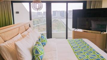 A hotel room with a large bed, a television, and a view of a cityscape through large windows.