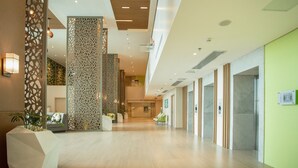 Un vestíbulo amplio con diseño moderno, que cuenta con un área de estar central, paneles decorativos y un ambiente luminoso y acogedor.