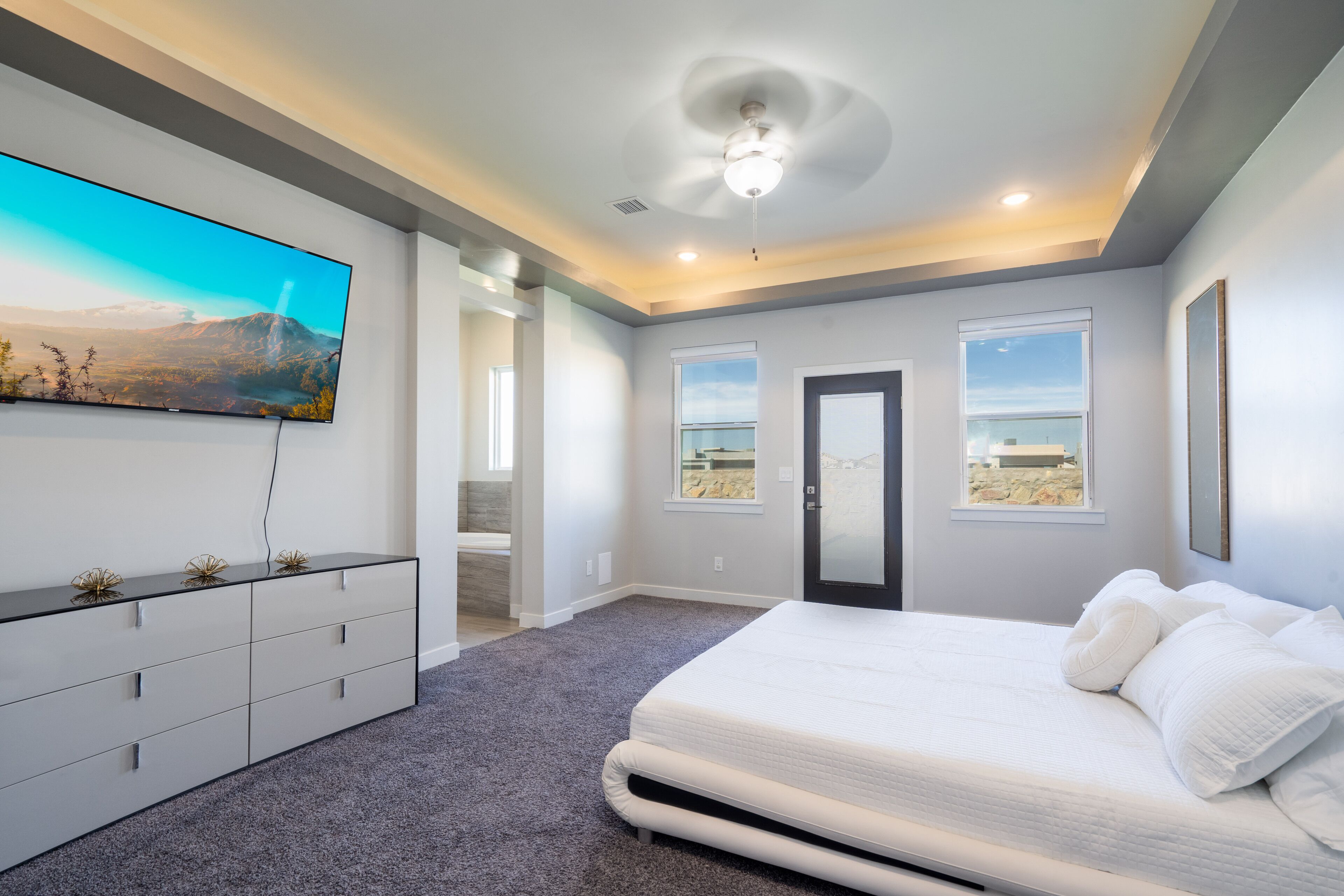 Un dormitorio con una cama grande, un televisor de pantalla plana montado en la pared y una puerta que da a otra habitación.
