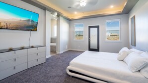 Ein Schlafzimmer mit einem großen Bett, einem flachbildfernseher an der Wand und einer Tür zu einem anderen Raum.