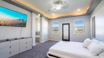 Un dormitorio con una cama grande, un televisor de pantalla plana montado en la pared y una puerta que da a otra habitación.