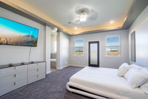Ein Schlafzimmer mit einem großen Bett, einem flachbildfernseher an der Wand und einer Tür zu einem anderen Raum.