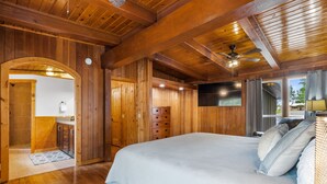L’intérieur d’une cabane en bois, avec un grand lit, un ventilateur de plafond et une vue sur l’extérieur.