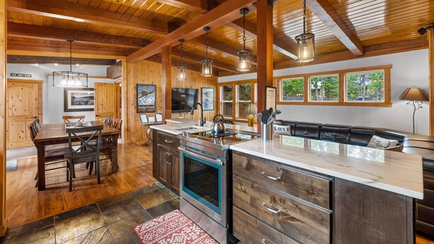Une cuisine spacieuse avec des poutres en bois, un grand îlot central doté d’un évier et un coin repas avec des chaises et une table.