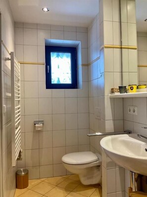 Ein kleines Badezimmer mit Toilette, Waschbecken, Fenster und Spiegel.