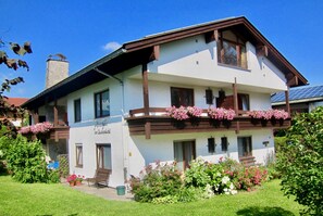 Ein zweistöckiges Gebäude mit Balkon, Schornstein und einem Ziergarten mit Blumen.
