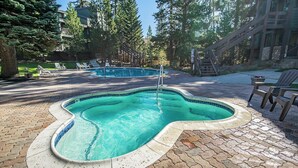 Ein Pool mit ungewöhnlicher Form, umgeben von einer Pflasterfläche und Bäumen.