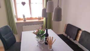 A dining table with a white tablecloth, two wine glasses, a bottle of wine, and a vase with flowers. There are two chairs and a sofa in the room. - Vacation apartment Kräuterbeet for 2 persons, 25 sqm, kitchenette, double bed (Inzell)