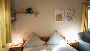 A cozy room with a wooden ceiling, a bed with white bedding, a nightstand with a lamp, and a small shelf with decorative items. - Vacation apartment Kräuterbeet for 2 persons, 25 sqm, kitchenette, double bed (Inzell)