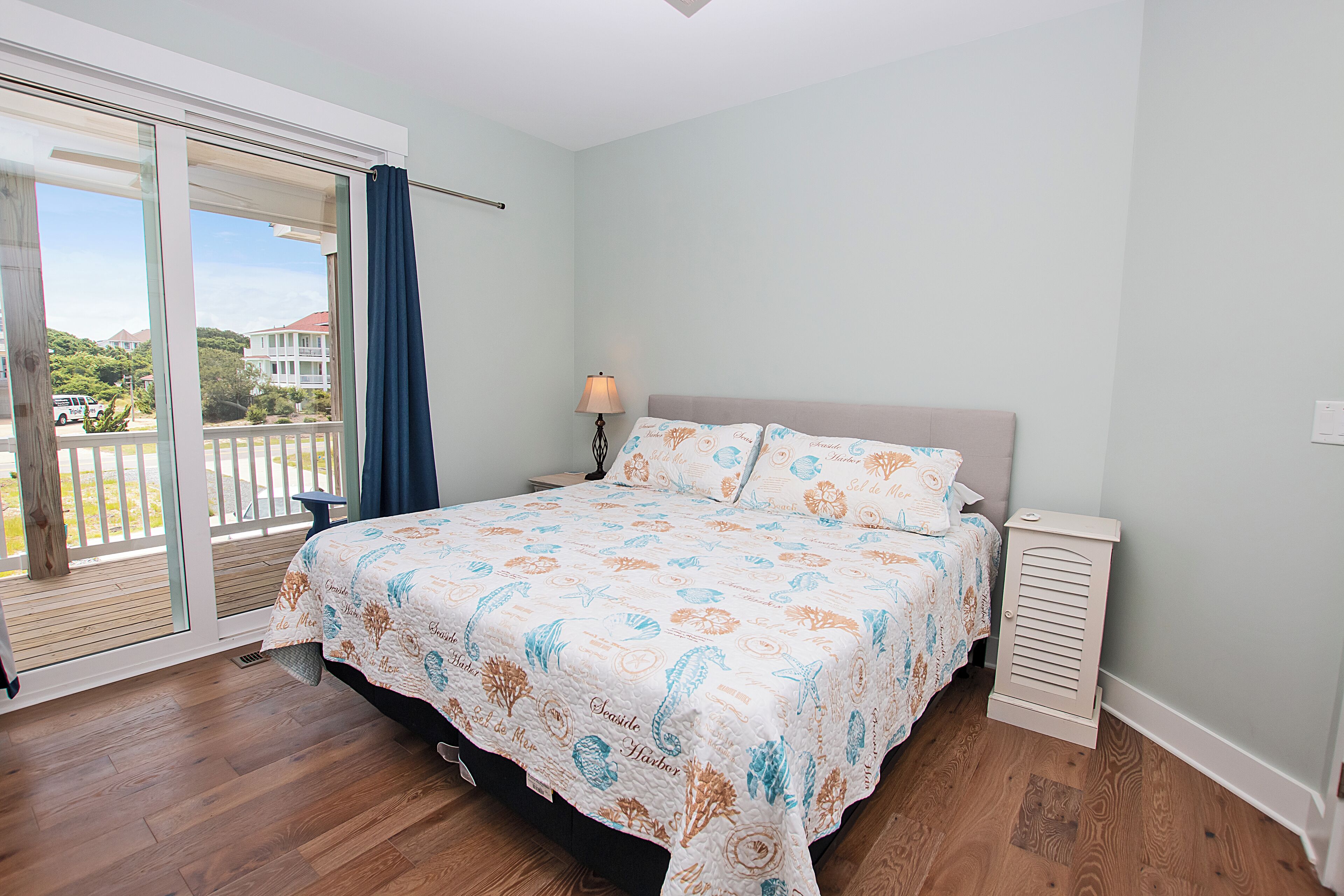 A bedroom with a large bed, a nightstand, a lamp, and a view of a balcony.