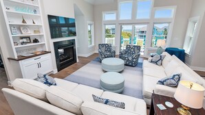 A living room with a fireplace, white sofas, ottomans, and a TV. - Oceanside, Private Pool, ELEV, Hot Tub Rec Room, yard, SUN-SUN, WW865-This One's for You! (Corolla)