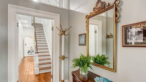 Una escalera que sube a un segundo piso, un espejo grande y ornamentado, y un mueble de madera con una planta.